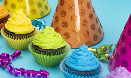 Rainbow Colored Frosted Chocolate Cupcakes on a Teal Background