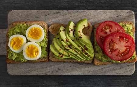 Three Varieties of Avocado Toast on a Dark Wood Tableの写真素材