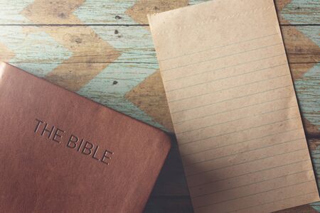 The Holy Bible on a Rustic Wooden Table with a Blank Piece of Antique Paper for Adding Textの写真素材