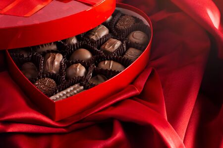 A Box of Milk Chocolates in a Red Love Heart on a Bed with Red Silk Sheetsの写真素材