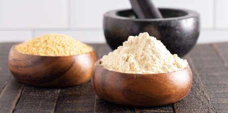 Bowls of Whole Millet and Millet Flour in Wood Bowls on a Dark Wood Tableの写真素材