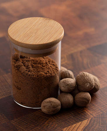 Jar of Ground Nutmeg and Whole Nutmeg on a Wooden Tableの写真素材