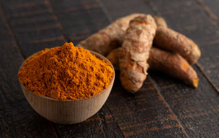 Bowl of Ground Turmeric on a Dark Wooden Tableの写真素材