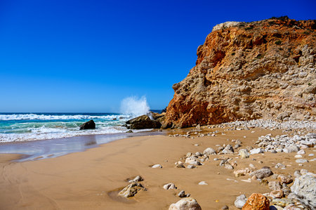 A beach with high rough cliffs at the Algarve in Portugal with some powerful waves.の写真素材