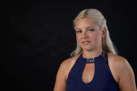 A very pretty young blonde lady in a sleeveless blue dress against a black background.の写真素材