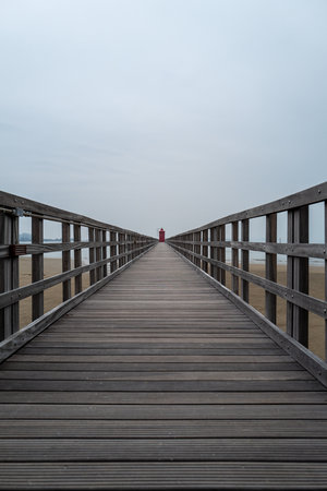 Small red old lighthouse at the end of a long jetty from a low perspective.の写真素材