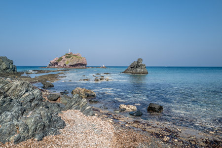 A beach by the sea with gravel and coarse boulders as well as a small island in the background.の写真素材