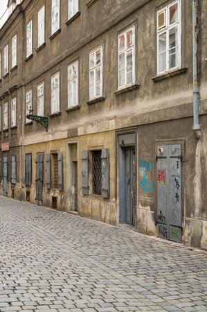 An old building with many windows and doors, some covered with graffiti, lines a cobblestone street. The building's facade shows signs of age and wear.の写真素材
