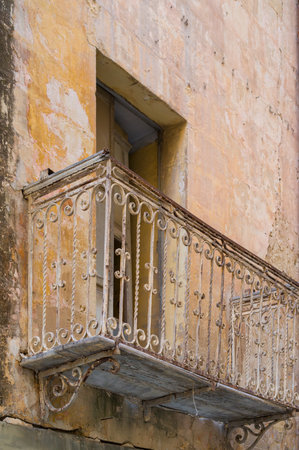 A weathered balcony with ornate ironwork clings to a crumbling facade. The peeling paint and rusted metal hint at a bygone era, evoking a sense of faded grandeur.の写真素材