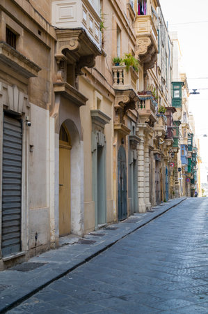 A narrow street in Valletta, Malta, showcases the city's unique architecture. Ornate balconies line the street, adding character and charm to the historic buildings.の写真素材