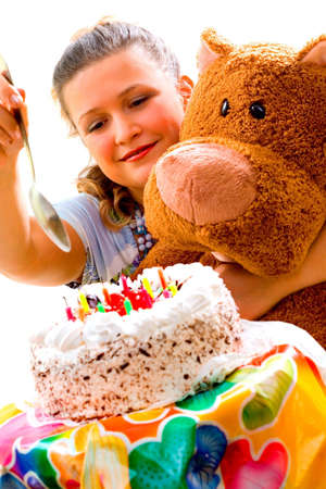 Girl tasting a birthday cake with teddy bear