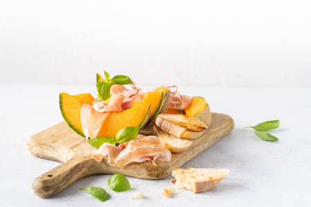 Fresh melon with prosciutto and basil. Antipasti, Italian food. Top view on white stone table with copy space for your textの写真素材