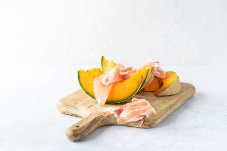 Fresh melon with prosciutto and basil. Antipasti, Italian food. Top view on white stone table with copy space for your textの写真素材