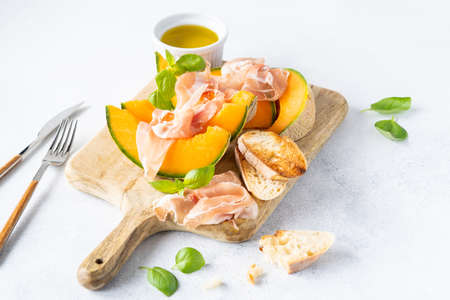 Fresh melon with prosciutto and basil. Antipasti, Italian food. Top view on white stone table with copy space for your textの写真素材