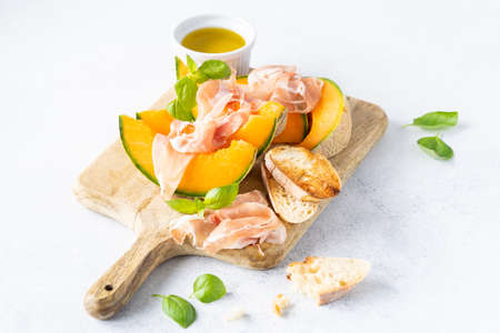 Fresh melon with prosciutto and basil. Antipasti, Italian food. Top view on white stone table with copy space for your textの写真素材
