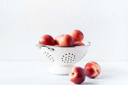 Fresh peaches and nectarines for a delicious Breakfast in a white iron bowl on a white background. The concept of delicious and healthy food. Copy space.の写真素材