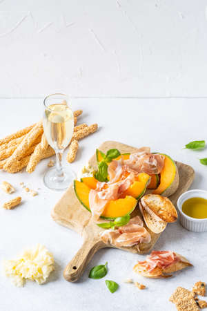 Fresh melon with prosciutto and basil. Antipasti, Italian food. Top view on white stone table with copy space for your textの写真素材