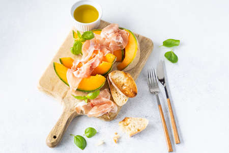 Fresh melon with prosciutto and basil. Antipasti, Italian food. Top view on white stone table with copy space for your textの写真素材