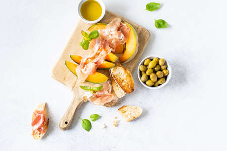Fresh melon with prosciutto and basil. Antipasti, Italian food. Top view on white stone table with copy space for your textの写真素材