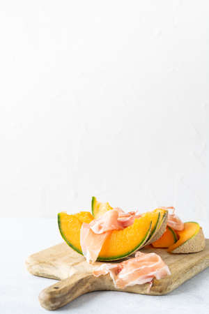 Fresh melon with prosciutto and basil. Antipasti, Italian food. Top view on white stone table with copy space for your textの写真素材