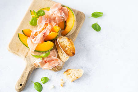 Fresh melon with prosciutto and basil. Antipasti, Italian food. Top view on white stone table with copy space for your textの写真素材