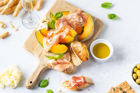 Fresh melon with prosciutto and basil. Antipasti, Italian food. Top view on white stone table with copy space for your textの写真素材