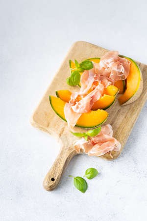 Fresh melon with prosciutto and basil. Antipasti, Italian food. Top view on white stone table with copy space for your textの写真素材