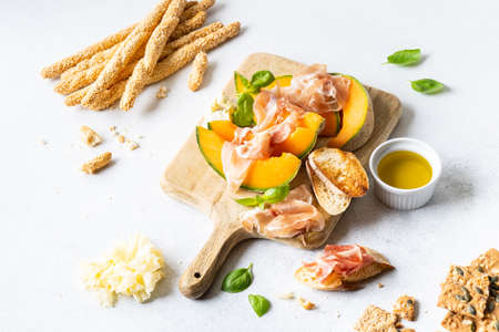 Fresh melon with prosciutto and basil. Antipasti, Italian food. Top view on white stone table with copy space for your textの写真素材