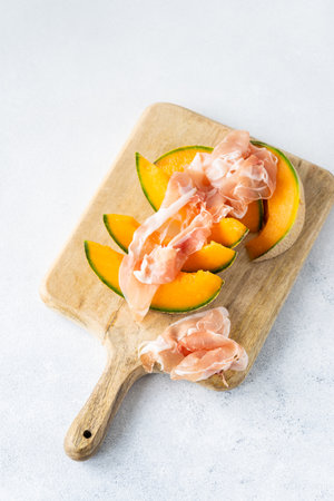 Fresh melon with prosciutto and basil. Antipasti, Italian food. Top view on white stone table with copy space for your textの写真素材