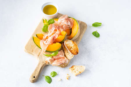 Fresh melon with prosciutto and basil. Antipasti, Italian food. Top view on white stone table with copy space for your textの写真素材