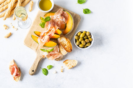 Fresh melon with prosciutto and basil. Antipasti, Italian food. Top view on white stone table with copy space for your textの写真素材