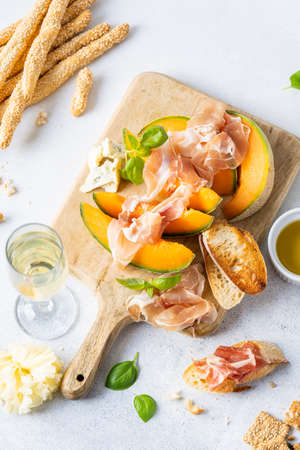 Fresh melon with prosciutto and basil. Antipasti, Italian food. Top view on white stone table with copy space for your textの写真素材