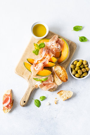 Fresh melon with prosciutto and basil. Antipasti, Italian food. Top view on white stone table with copy space for your textの写真素材
