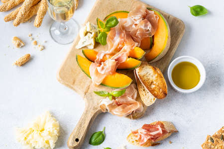 Fresh melon with prosciutto and basil. Antipasti, Italian food. Top view on white stone table with copy space for your textの写真素材