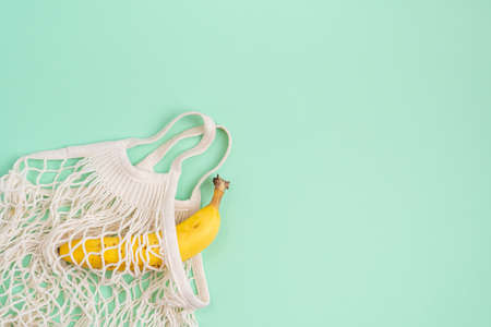 Yellow banana in an eco string bag on a colored background.Eco-friendly kitchen accessories.の写真素材