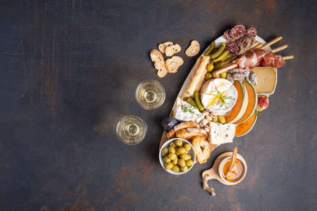 Snacks table with Italian snacks and wine in glasses. Brushetta, a kind of cheese board on a black background. Top view, flat layerの写真素材