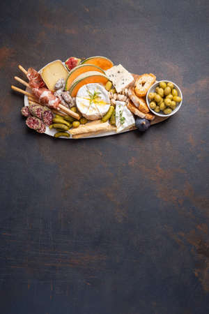 Assorted cheeses on wooden board plate, olive, grapes, bread on black stone background, top view, flat lay, copy space.の写真素材