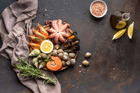 A mix of seafood on a plate. Fish, octopus, squid, shrimp, snails, lemon and herbs on a black...