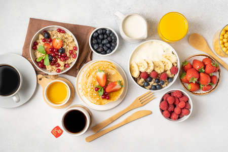 A table for a healthy breakfast of pancakes, granola, fresh berries, coffee with milk and orange juice. Top view.の写真素材
