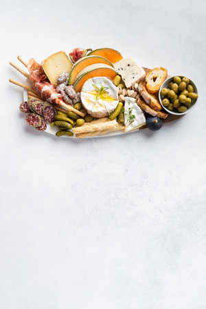 Assorted cheeses on wooden board plate, olive, grapes, bread on white background, top view, flat lay, copy space.の写真素材