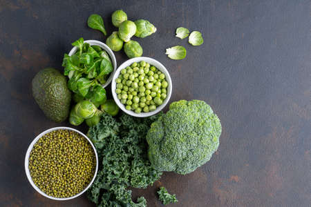 Healthy vegetarian food concept background, fresh green food selection for detox diet, raw broccoli, apple, spinach, peas, avocado, lime, corn salad, top viewの写真素材