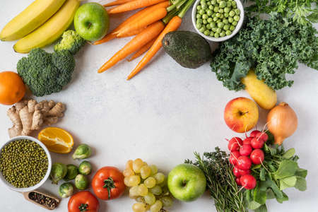 Variety of raw green vegetables salads, carrots, tomatoes, bananas, peas, corn, broccoli, savoy cabbage as frame round empty white chopping board. Food background. Top view, space for textの写真素材