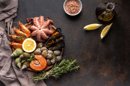 A mix of seafood on a plate. Fish, octopus, squid, shrimp, snails, lemon and herbs on a black background.の写真素材