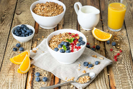Healthy lifestyle in a breakfast plate with muesli and a spoon on the background of a brown wooden table with milk, berries and orange juice. organic muesli, morning diet for health conceptの写真素材
