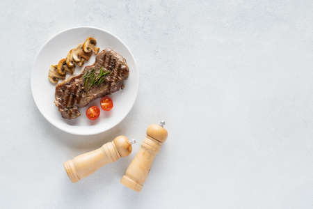 Grilled beef steak with mushrooms and spices on a white ceramic plate. Top view, copy space