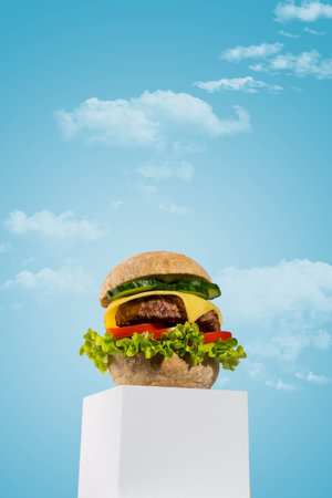 A delicious, freshly made homemade cheeseburger is presented on a minimalist white podium against a soft blue background.の写真素材