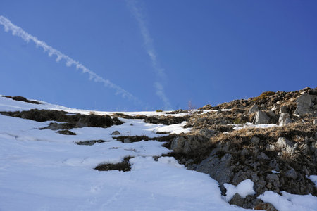 Snowy mountain slope under clear blue sky with contrailsの写真素材