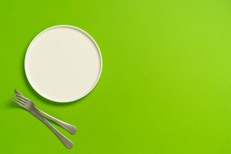 Empty white plate with fork and knife on green background.の写真素材
