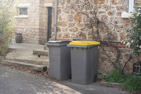 Garbage bins lined up near stone residential wall.の写真素材