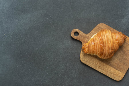 Freshly baked croissant on wooden cutting board against dark background. High quality photoの写真素材